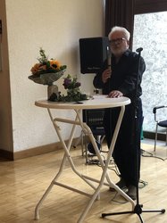 Klaus Peter Murawski steht an einem Stehtisch und hält eine Rede. Blumendeko auf dem Stehtisch.